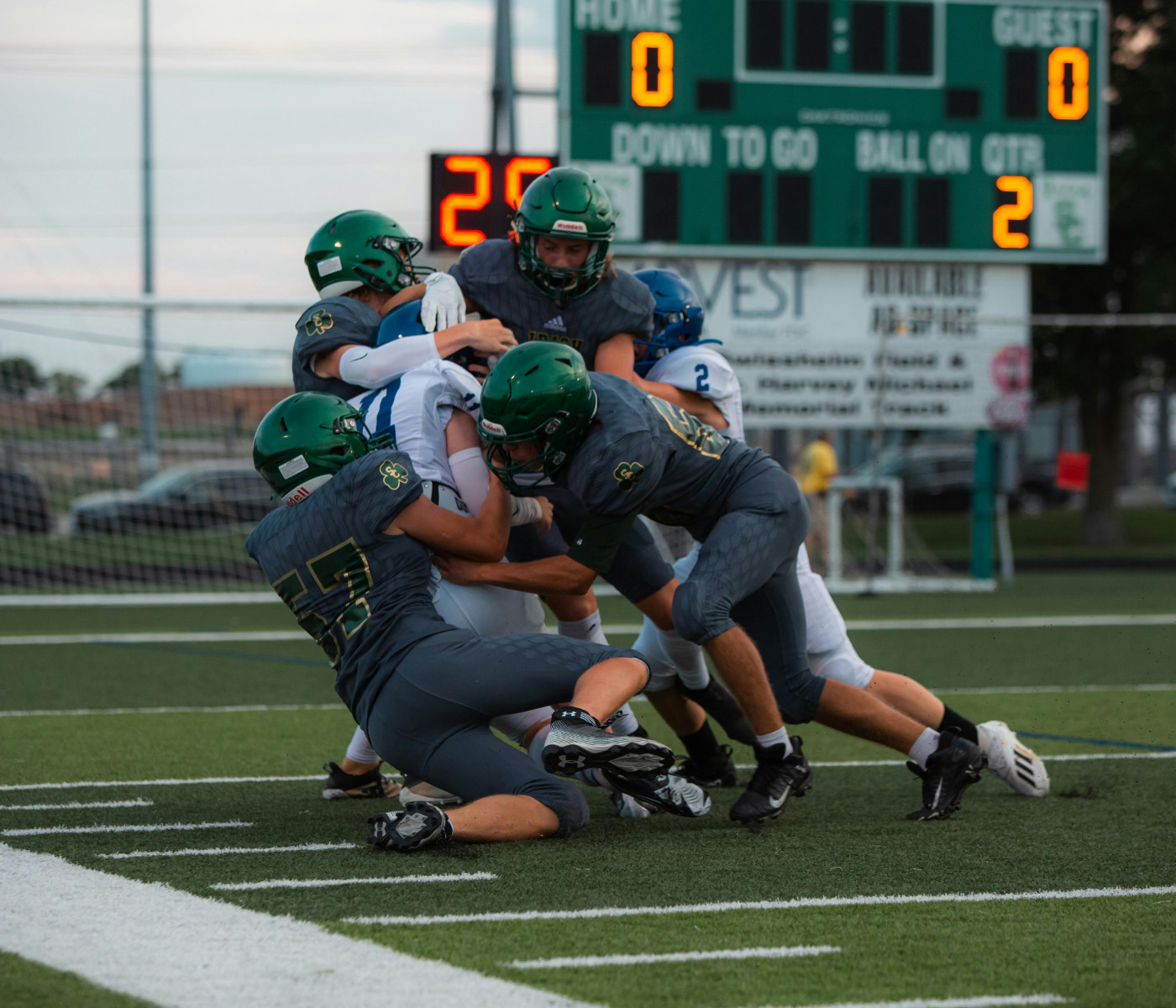 High school football game action shot, defenders in green uniforms tackling the ball carrier near the goal line